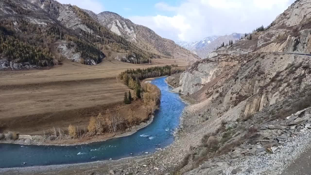 从山顶俯瞰风景如画的山谷，周围群山环绕，蜿蜒流淌着绿松石色的河流。视频素材