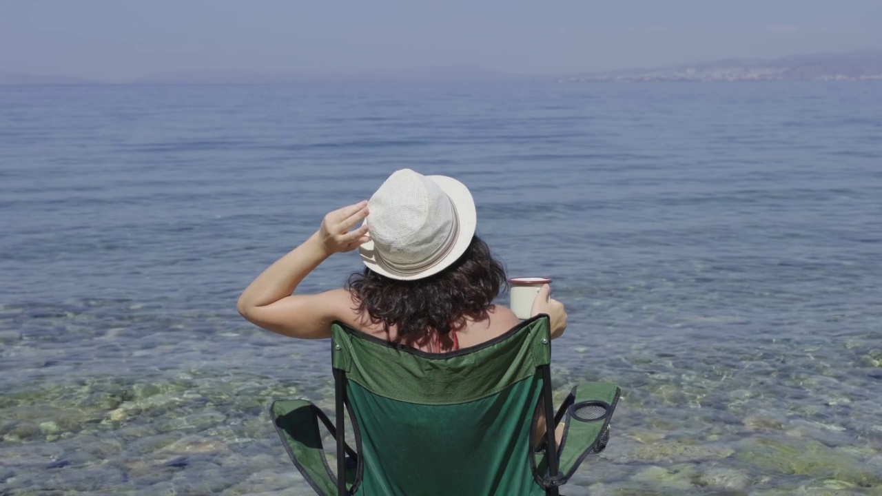 在露营的海边喝咖啡的年轻女子。旅行者游客比基尼女人女孩在帽子放松假期快乐的假期视频素材