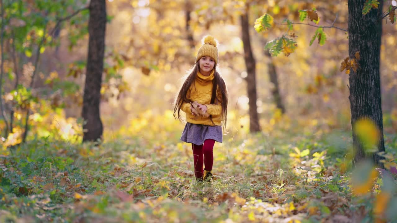 在一个阳光明媚的秋日里，快乐的女孩在森林里玩着秋叶的颜色。无忧无虑的女子在公园小路上奔跑，秋天风景4k视频视频素材