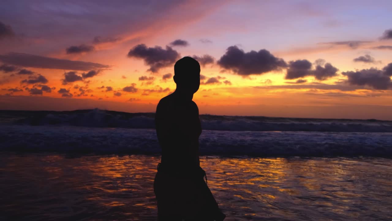 夕阳下漫步在海滩上的男人剪影，度假时再造热带岛屿，轻松的生活方式。傍晚，人们在海边散步，欣赏着美丽炽热的日落视频素材