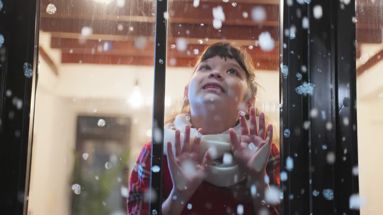 可爱的孩子透过窗户欣赏着初雪。小女孩坐在家里的客厅里，看着外面飘落的雪花享受着与家人一起庆祝圣诞节、感恩节。视频素材