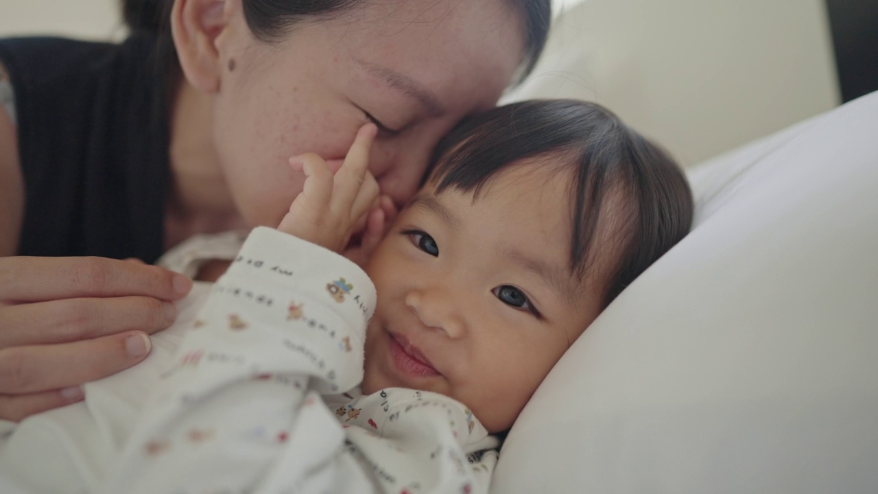 在亚洲母亲第二次怀孕的舒适卧室里，她正高兴地亲吻着女儿。视频素材