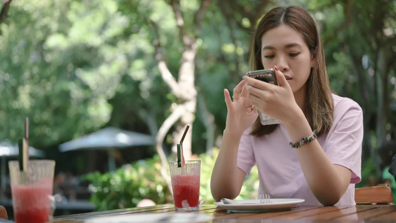 一名东南亚女子在户外咖啡馆边看手机边等意大利菜视频素材