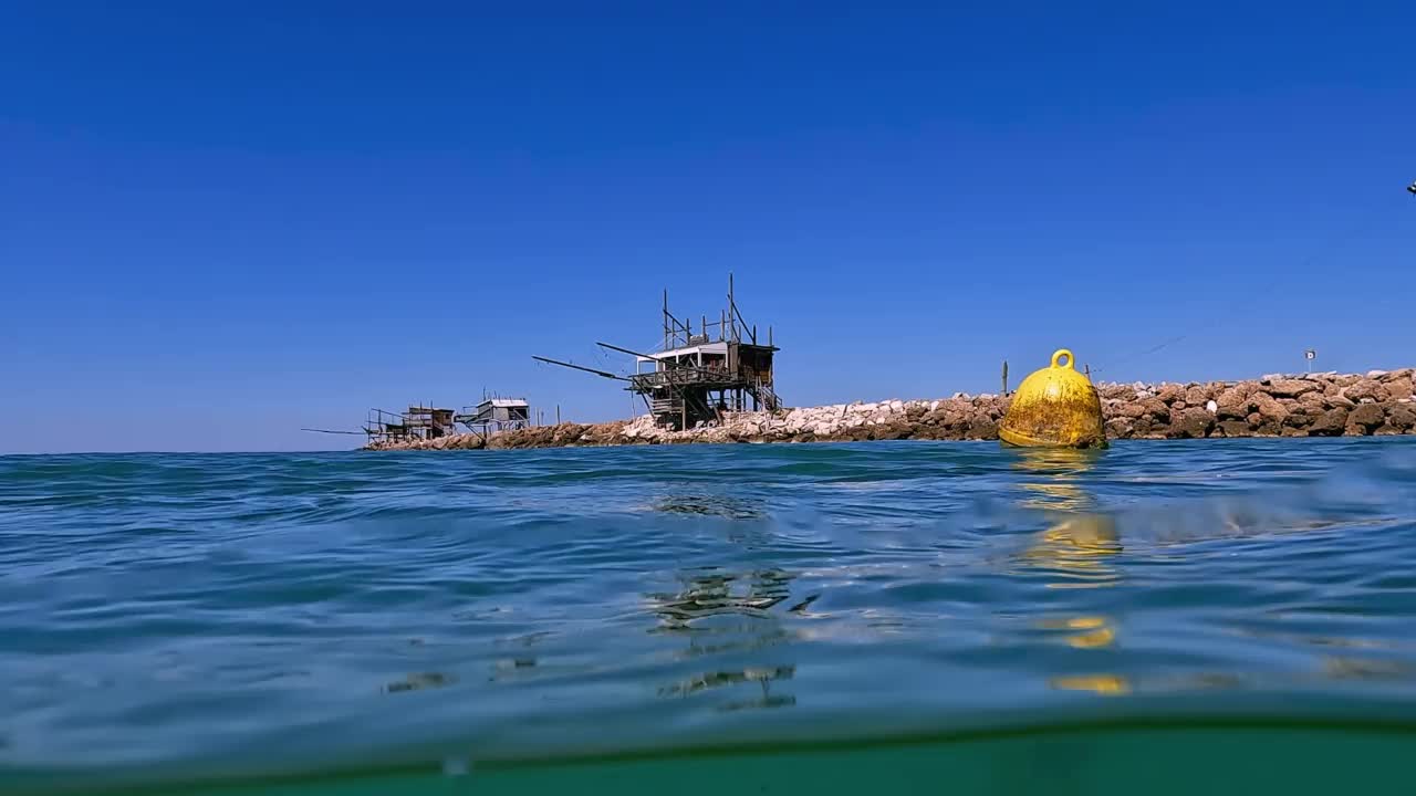 半水下翻拍的黄色浮筒和木制钓鱼平台在岩石防波堤的背景。意大利的Abruzzo视频素材