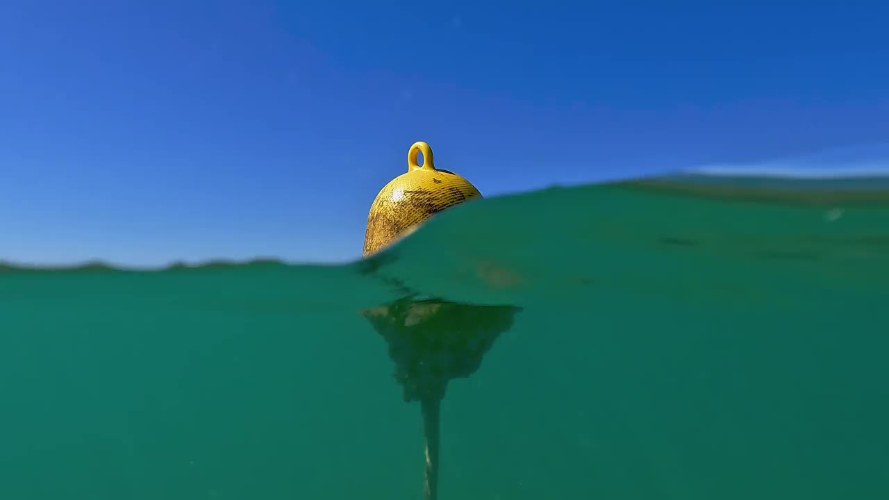 半水下倾斜从海底到水面的黄色漂浮系泊浮标的海水。慢动作视频素材