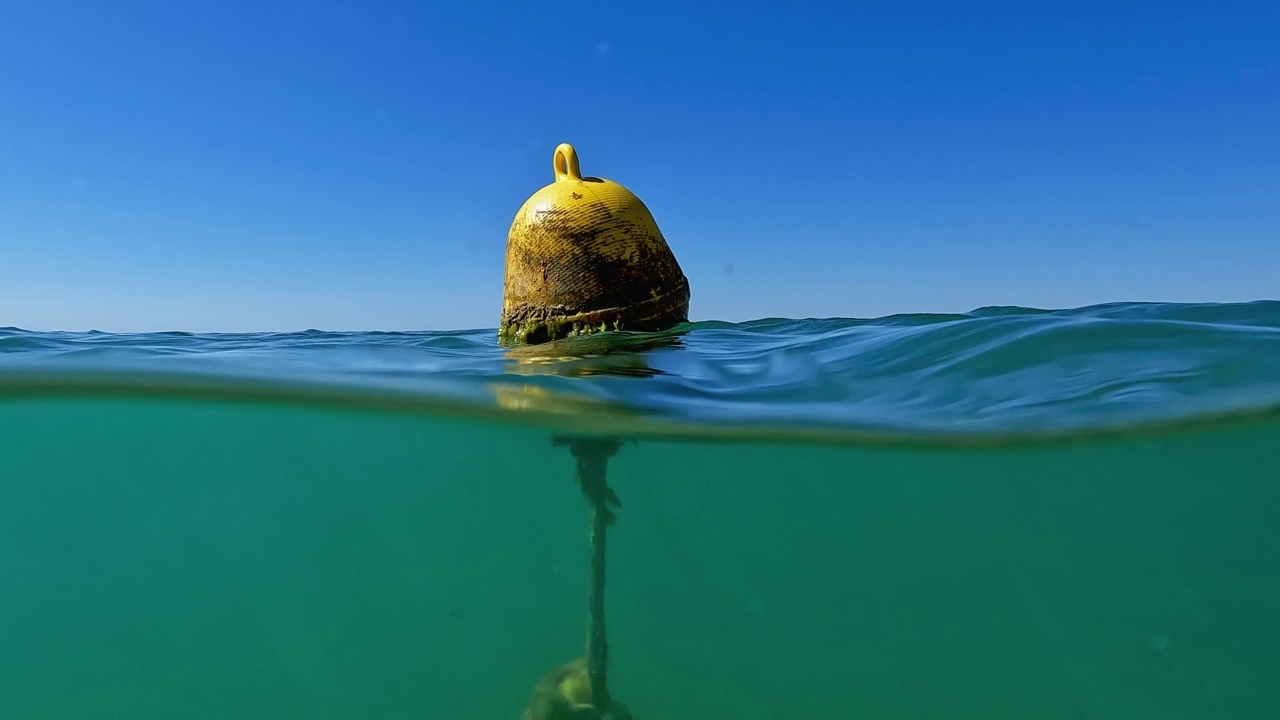 半水下倾斜从海底到水面的孤立黄色漂浮系泊浮标的海水。慢动作视频素材