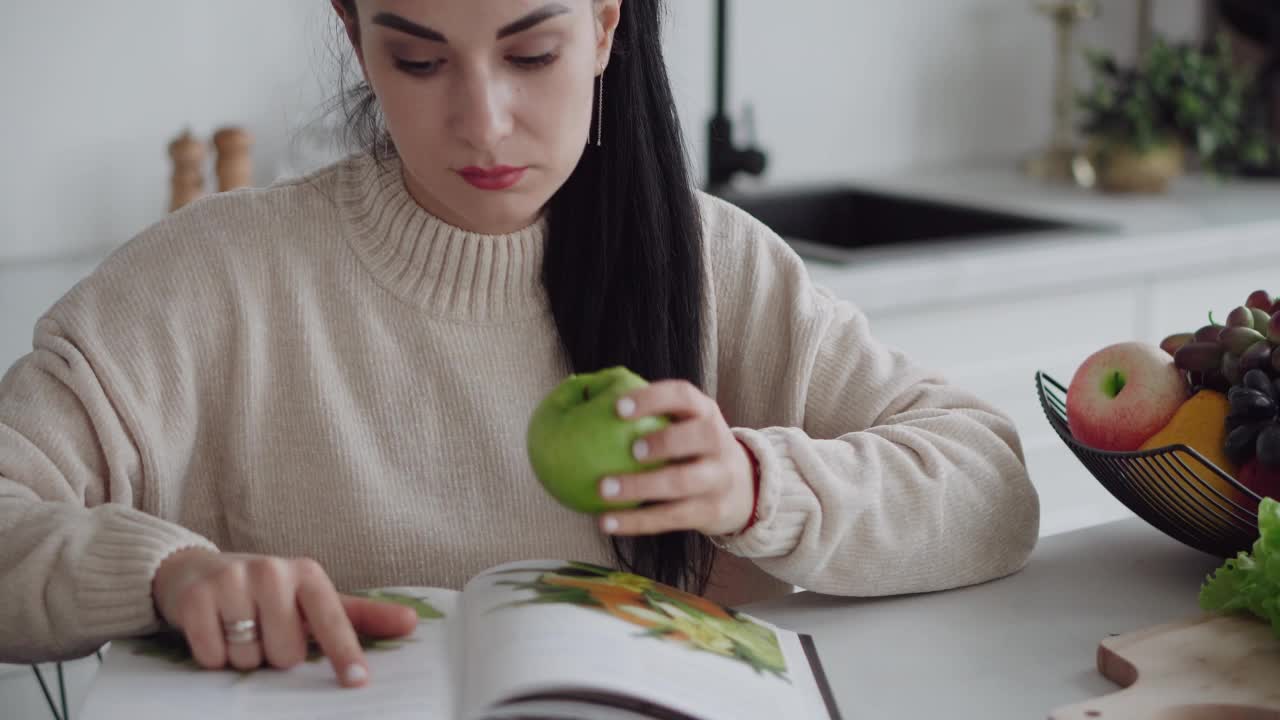 一位年轻女子正在节食。这位女士是素食主义者。读一本关于健康饮食和生活方式的杂志。健康饮食。一个年轻女人吃很多绿色蔬菜。自我保健。一位女士正在阅读一本关于饮食和健康饮食的杂志。视频素材