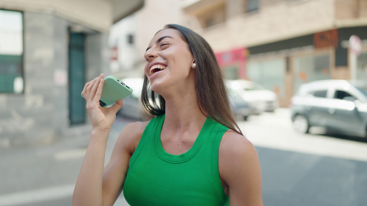 年轻美丽的西班牙女人微笑着自信地在街上用智能手机说话视频素材