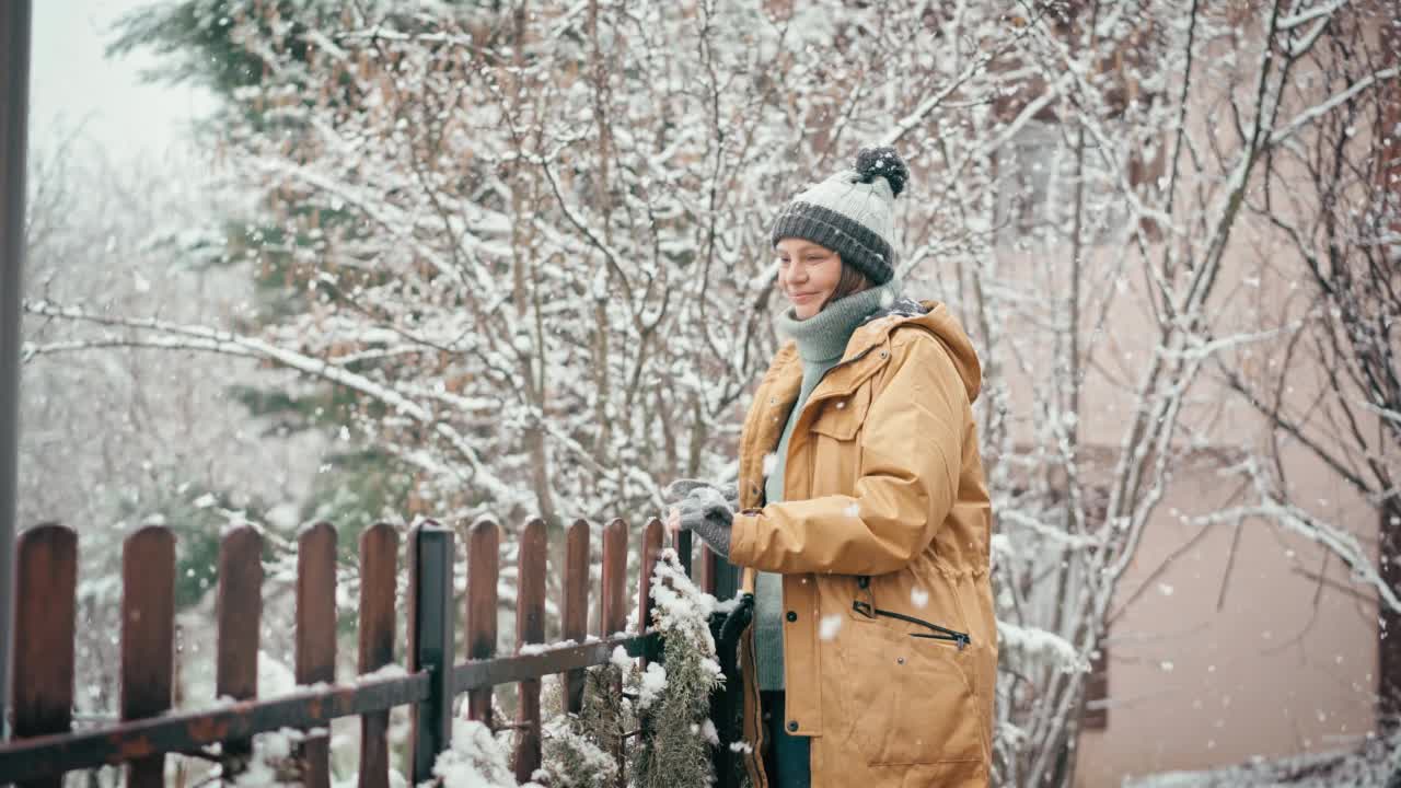 一位妇女站在乡间别墅的露台上享受降雪。视频素材