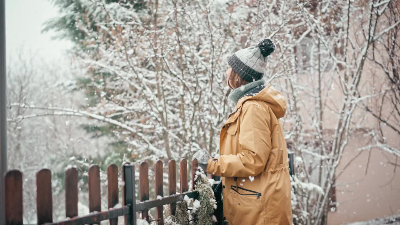 一位妇女站在乡间别墅的露台上享受降雪。视频素材