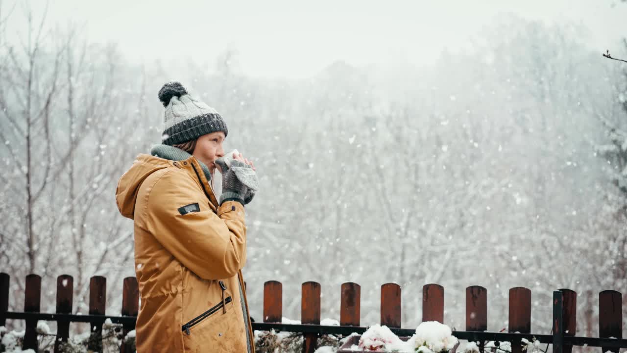 一位女士一边享受大雪，一边用杯子喝着热饮视频素材