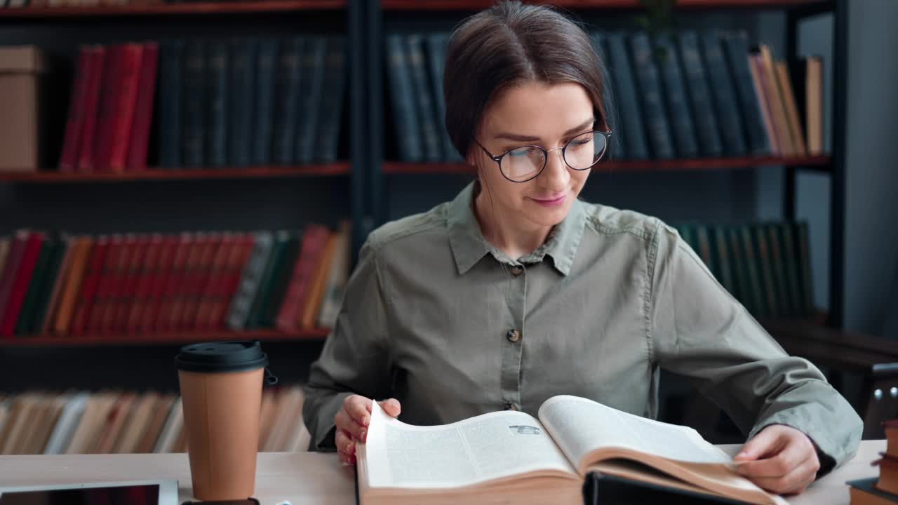 微笑的美女在公共图书馆的桌子上看书翻纸考试大学讲座视频素材