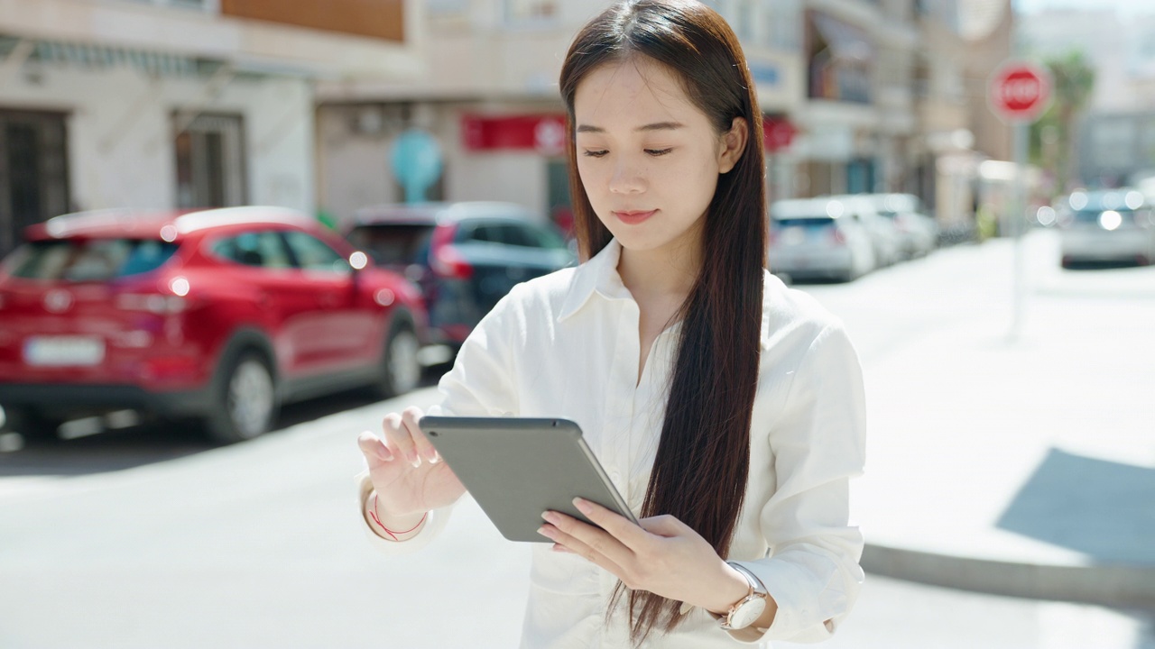 年轻的中国女子自信地微笑着在街上使用触摸板视频素材