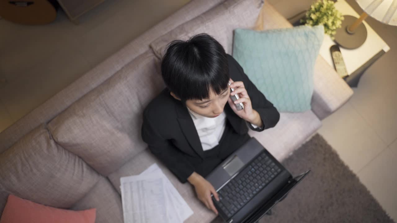 高角度拍摄了一位坐在沙发上看电脑的女商人，晚上挂了电话，张开双臂紧握拳头欢呼成功。视频素材