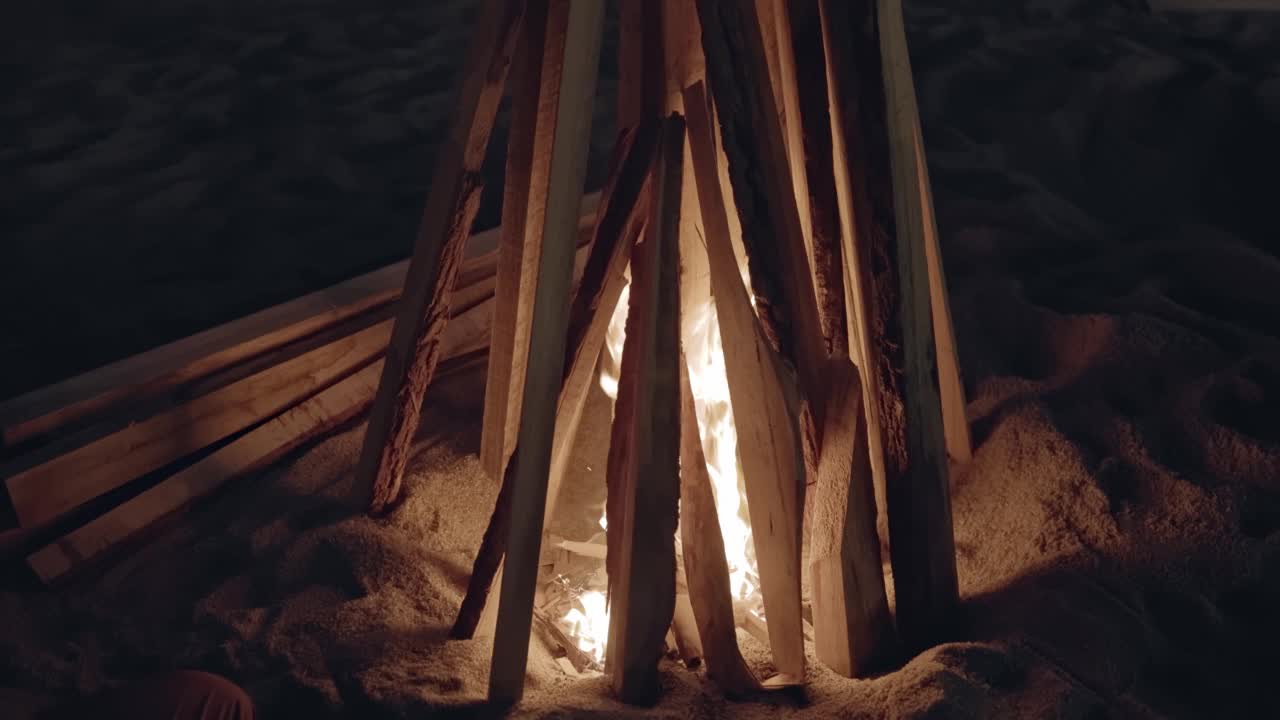 夜晚，在大自然的一堆篝火中，一个女孩的手正在烤一根棍子上的食物。视频素材