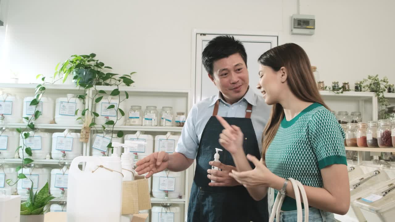 亚洲男店主在补充店为女顾客补充液体产品。视频素材