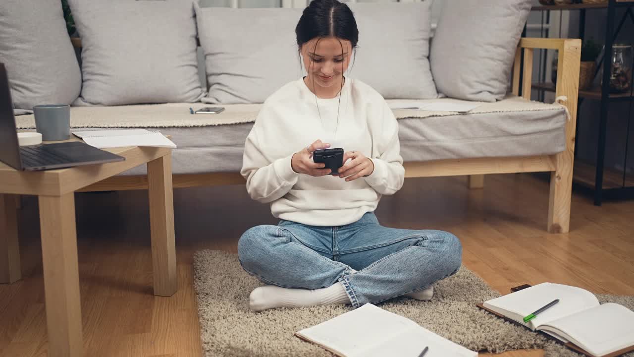 女学生坐在地板上用智能手机寻求作业帮助视频素材