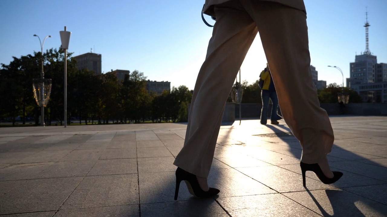 女性穿着高跟鞋走在城市街道上，背景是太阳耀斑。年轻的女商人穿着高跟鞋走在城市里。女孩走路去上班。慢动作视频素材