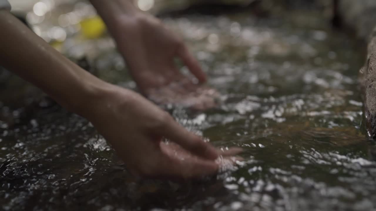 女游客在大自然中散步，遇到一条小溪。一个女孩的手接触水的特写。视频素材