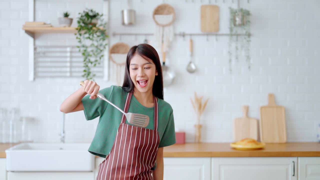 亚洲年轻女子在厨房里跳舞。女性在周末的空闲时间快乐和放松视频素材