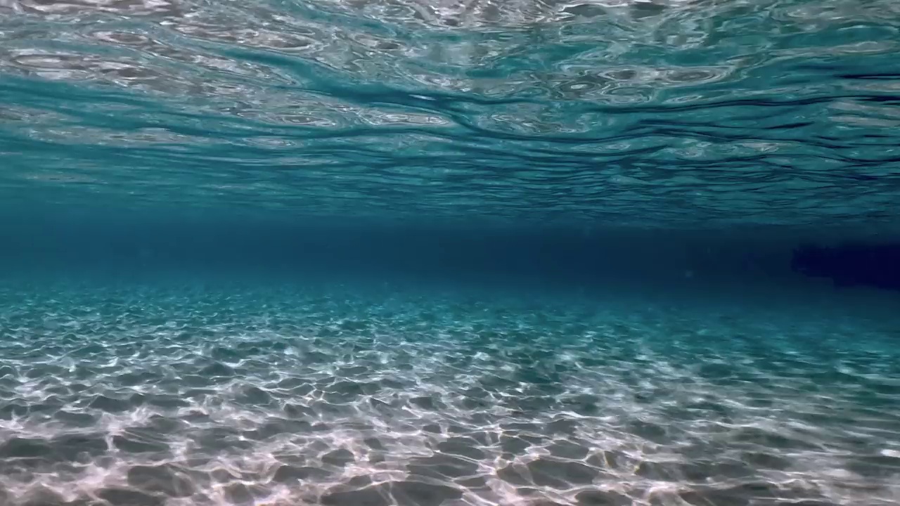 真实的水下场景结晶绿松石热带海水波纹表面和反射海底与蓝色背景。慢动作视频素材