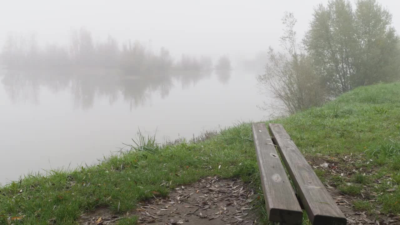 在一个雾蒙蒙的秋日，一张空木凳上的湖岸景色视频素材