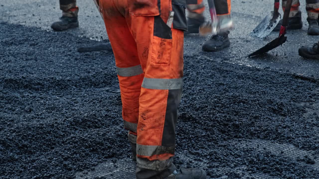 穿着防护服的道路工程工人正在用热沥青修补街道柏油路面视频素材