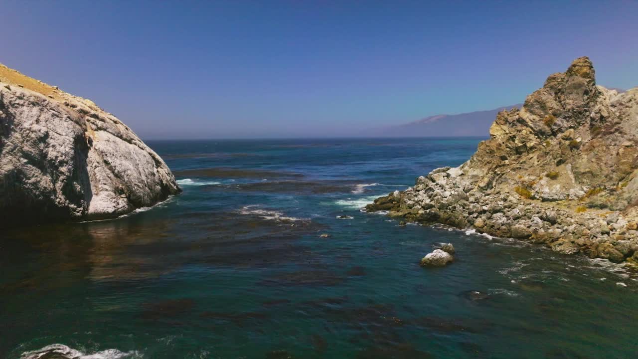 在太平洋蔚蓝的海面上低空飞行。水藻漂浮在水面上。加州的群山在朦胧的背景下。视频素材