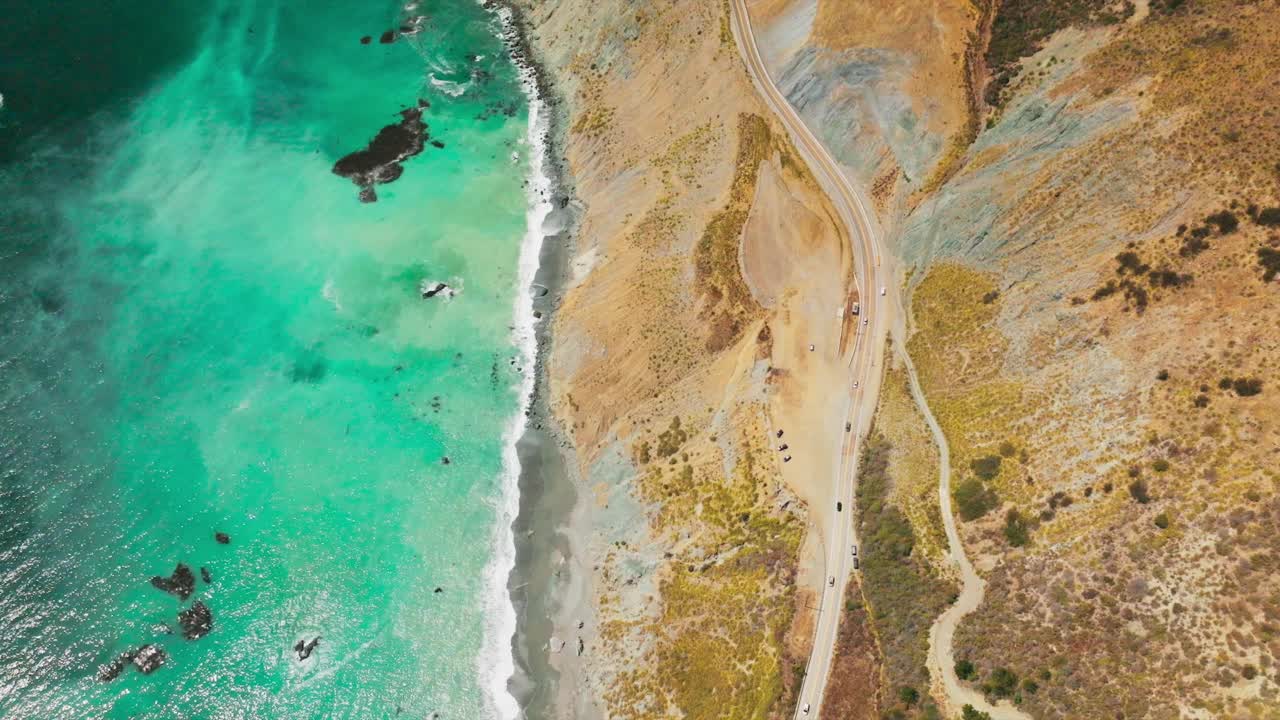 蓝绿色的海水与加利福尼亚的岩石海岸相遇。山顶高速公路的俯视图。视频素材