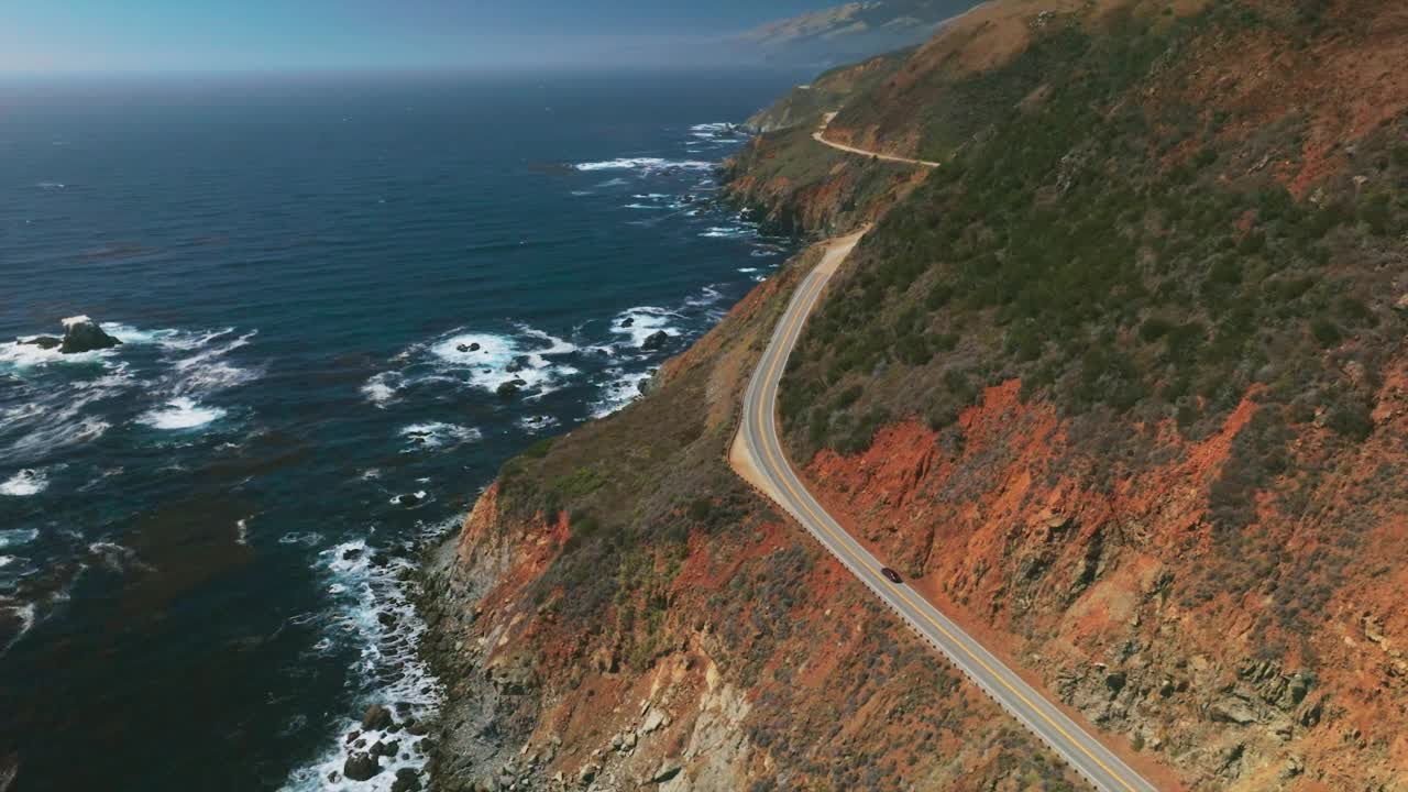 加州壮丽的山脉中间有高速公路。深蓝色的海洋和白色的泡沫波。空中的视角。视频素材