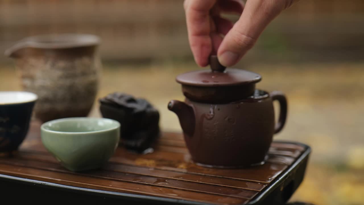 特写镜头。一只手合上了泡普洱茶的陶制茶壶的盖子。户外中国茶道视频素材