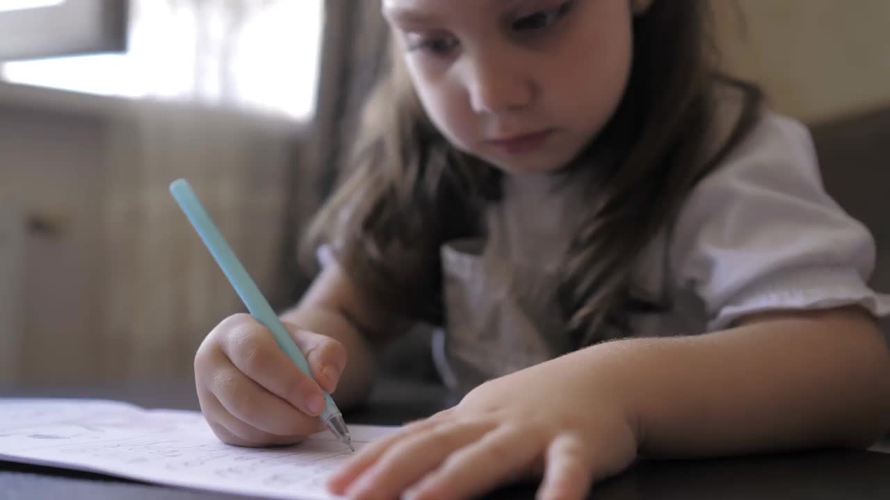 可爱聪明的5岁学龄前小女孩在作业本上写作业，学习字母，坐在家里的桌子上。为上学做准备。家庭远程教育。儿童学前概念视频素材