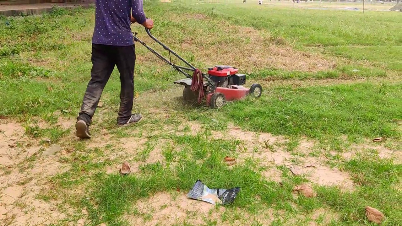 在加尔各答的一个操场上，一个男人用电动割草机割草的特写镜头。视频素材