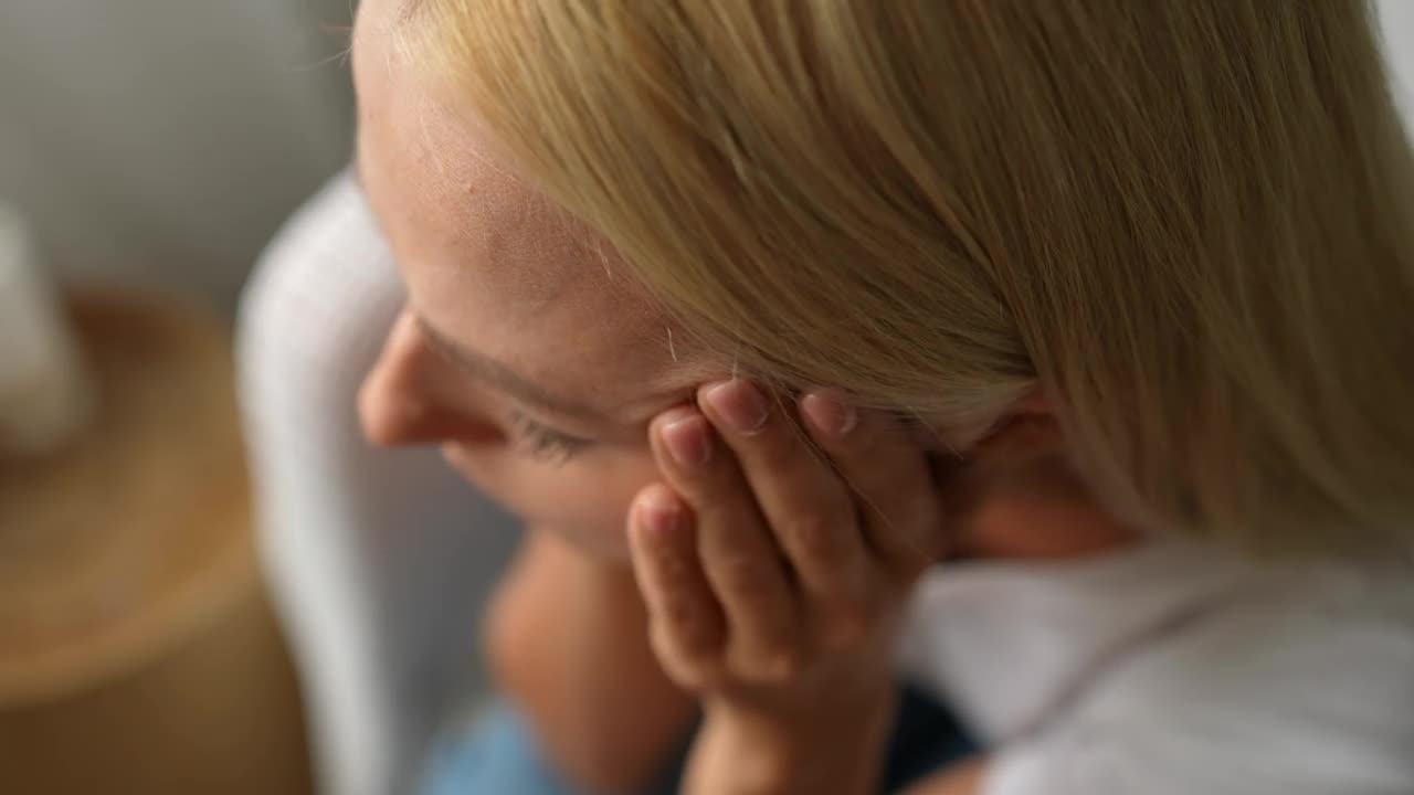 近景高角度观看不适的年轻女子坐在床上，摩擦太阳穴与闭上眼睛遭受头痛，疼痛的感觉。视频素材