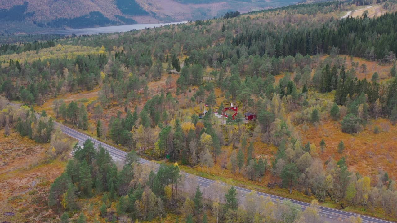 鸟瞰隐藏在挪威公路旁秋天森林中的红色山间小屋视频素材