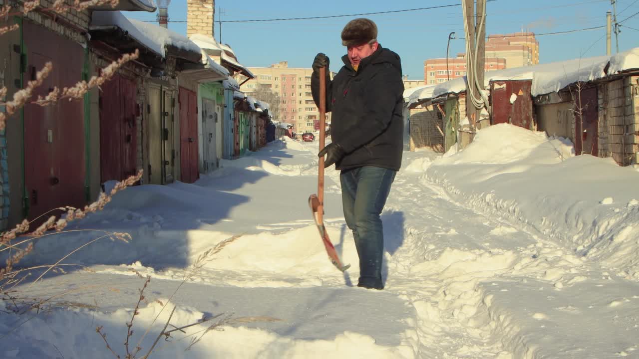 一个快乐的人用木铲清理通往车库的积雪。视频素材