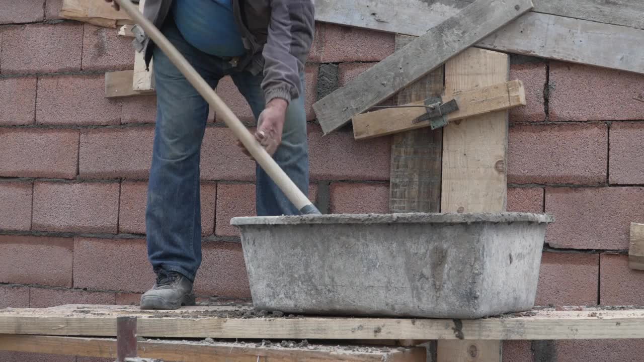 工地中段无名男子手持铁锹将水泥混凝土浇筑在建筑墙面上视频素材