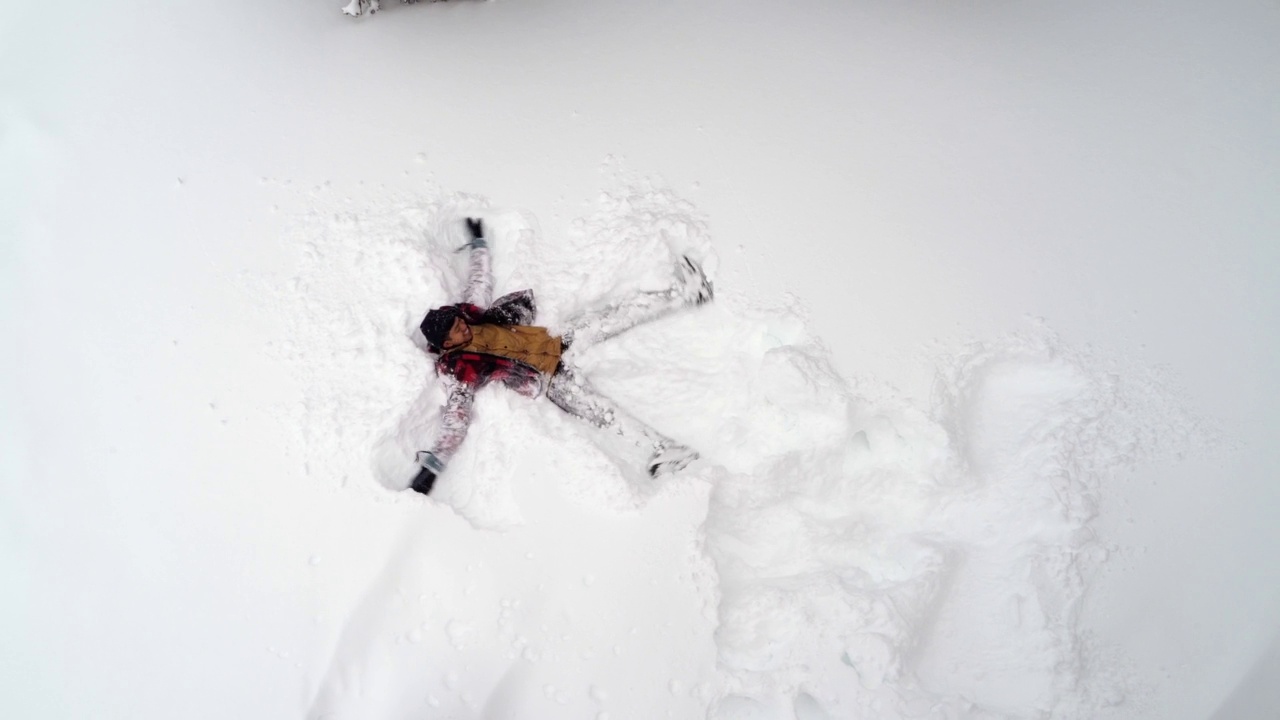 一名身穿红色夹克的男子在加拿大班夫的雪山上制作雪天使视频下载