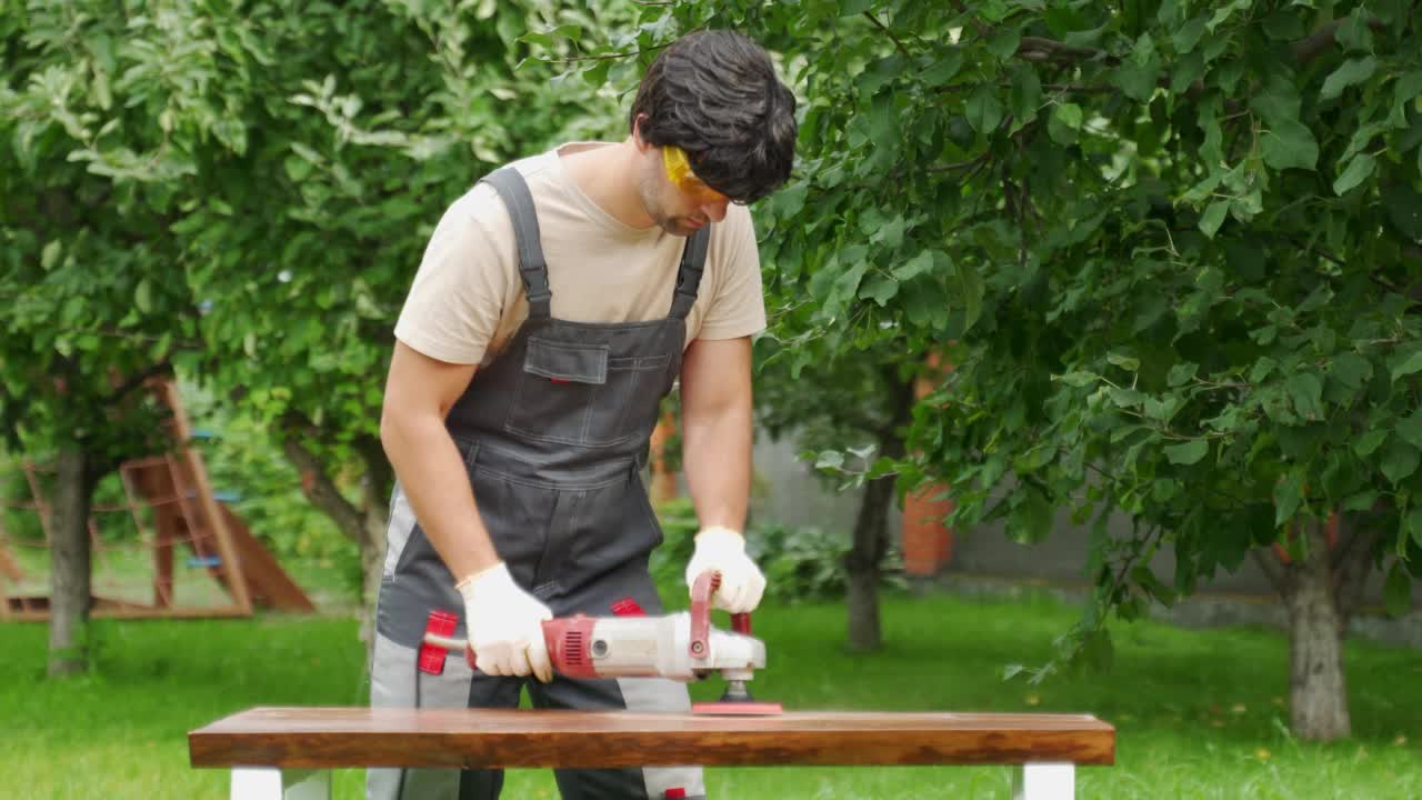 年轻的建筑工人木匠在后院用磨床磨一张木桌视频素材