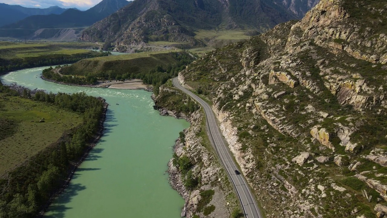 空中:蓝绿色的河流在山谷中流动，道路上有汽车视频素材