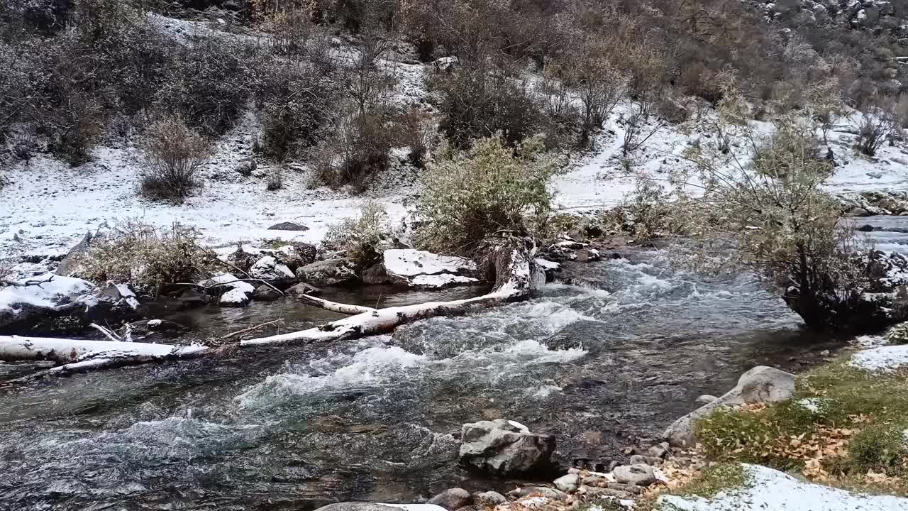 一条浅浅的河流从山上沿着覆盖着初雪的岩石河岸疾驰而下。视频素材