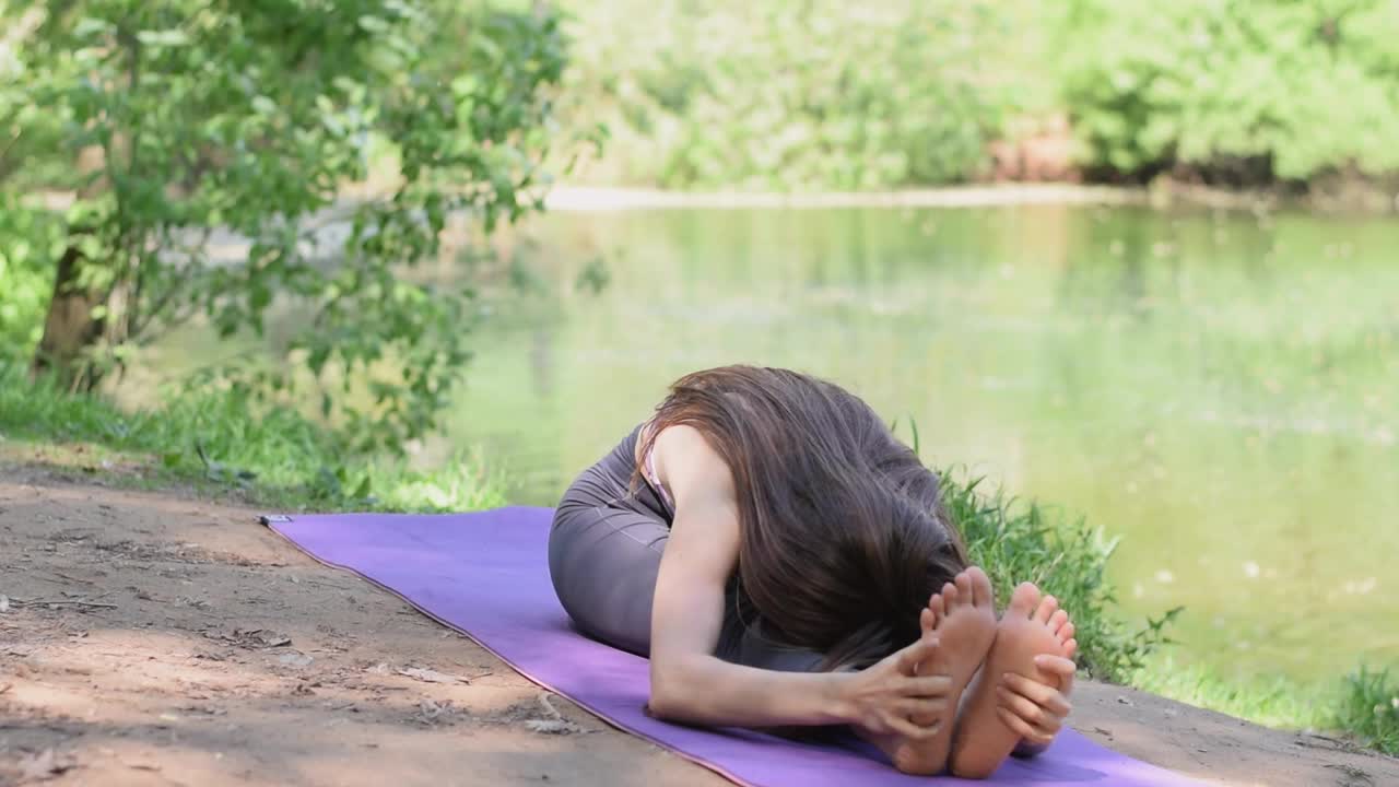 年轻的运动女性在一个夏天的户外练习瑜伽，坐在莲花位。放松和冥想。健康，幸福，心理健康的概念视频素材