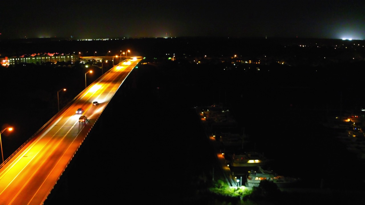 空中倒拍的汽车在高速公路上移动，无人机在夜晚飞过照亮的城市——佛罗里达州的代托纳海滩视频素材