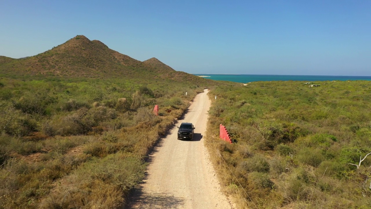 空中向后拍摄的汽车移动在道路上的自然景观中海洋在晴朗的天空-下加利福尼亚，墨西哥视频素材