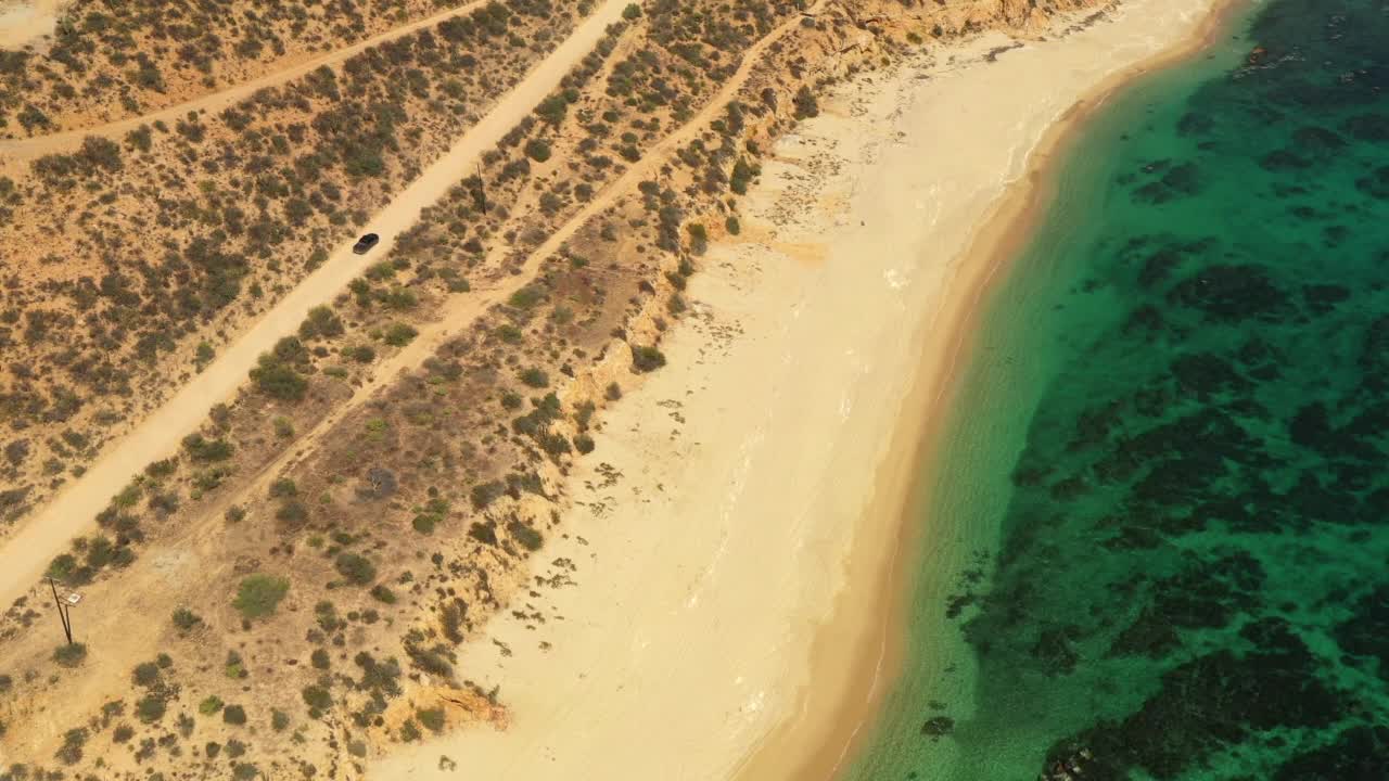 航拍的汽车在半干旱的土地中移动的道路上，无人机在蓝绿色海岸线的海滩上向前飞行-下加利福尼亚，墨西哥视频素材