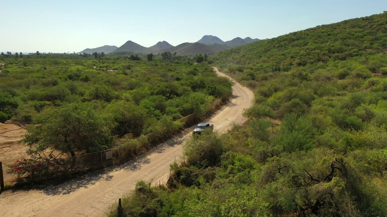 空中倒拍的汽车在道路上移动在绿色植物和晴朗的天空-下加利福尼亚，墨西哥视频素材