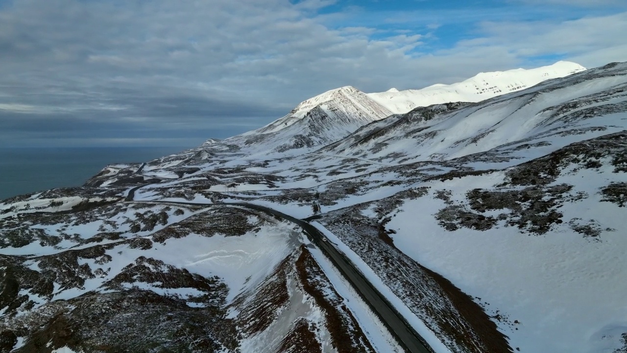 空中向前拍摄的车辆在多云天空下的雪山公路上行驶-冰岛瓦特纳冰盖国家公园视频素材