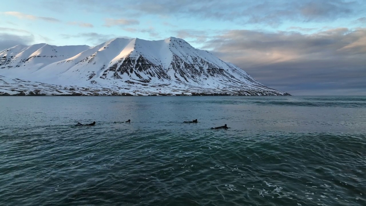 游客在多云天空下雪山旁的Jokulsarlon泻湖上用冲浪板游泳的封锁镜头——冰岛的Vatnajokull国家公园视频素材