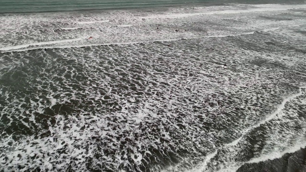 航拍的游客用冲浪板在海里游泳，无人机向后飞过黑沙滩-冰岛瓦特纳冰盖国家公园视频素材