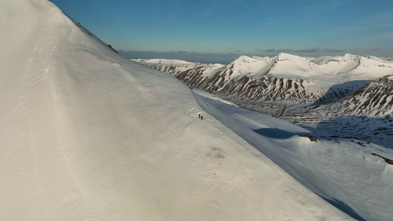 航拍的游客朋友在山坡上滑雪，无人机在阳光明媚的日子里从雪上向下飞行-冰岛的瓦特纳冰川国家公园视频素材